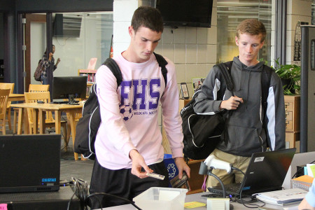Mitch Chambliss (12) and Daniel Eberle(11) drop their IDs into the bin as they enter the library after school.