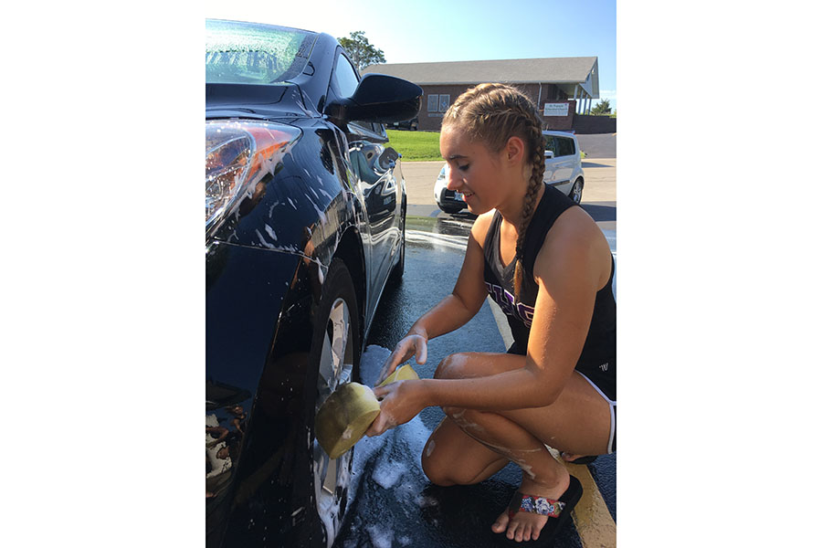 In charge of cleaning the wheels, Maddie Ripson (12), scrubs down some tires at the Golden Line Carwash at Farmer’s and Merchants Bank, Aug. 26. “The car wash made us closer as a team,” Ripson said. “It is a great opportunity to spend the day with my best friends. It provided as a great team bonding experience. It takes a lot of teamwork to wash a car, but it was a good time.” 