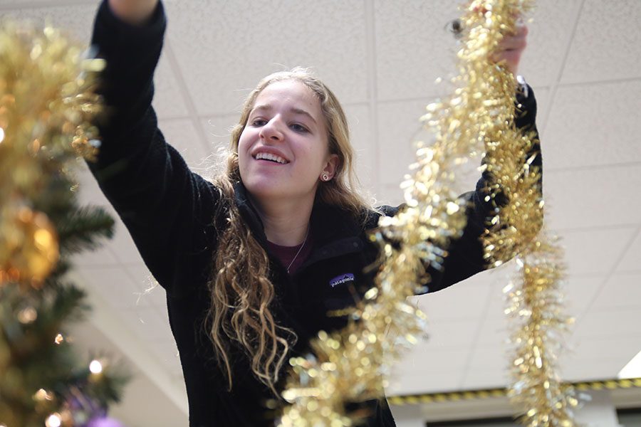 Tinsel being hung, Savannah Lesher (11) decorates holiday trees in the commons with StuCo after school, Dec. 3. “The holiday trees brings everyone together,” Lesher said. “It doesnt matter what religion or who you are, everybody can come together this time of the year and have a fun time. It exemplifies that everybody has different beliefs. They’re holiday trees so everybody can be involved.”