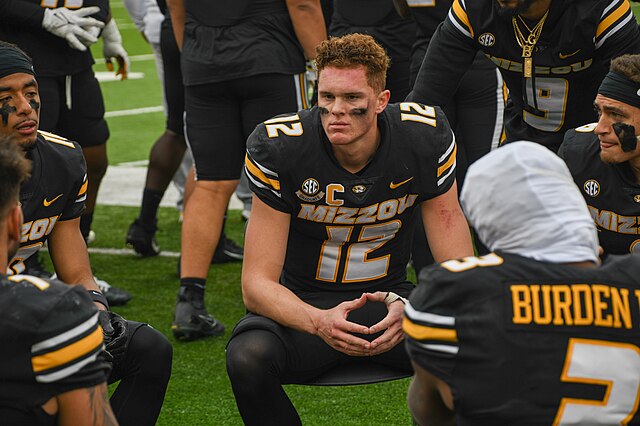 Brady Cook, University of Missouri, Columbia, quarterback, sits with teammates while Missouri's defense takes the field during the Veterans Day military appreciation football game against the University of Tennessee. Prior to the game, service members were honored with a ceremonial wreath presentation and a B-2 Spirit stealth bomber flyover during the U.S. national anthem. (U.S. Air National Guard photo by Tech. Sgt. Stephanie Mundwiller)