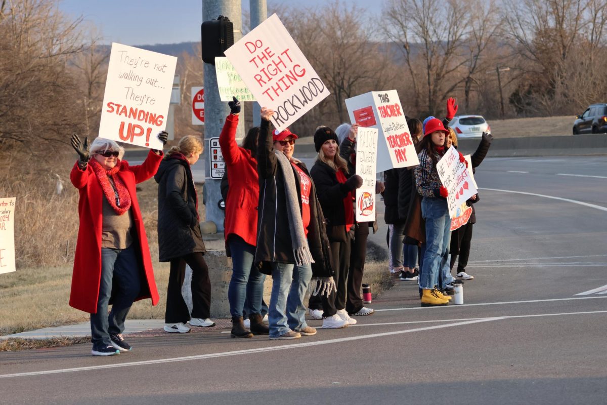 Dressed in red, community members hold up signs for passing cars alongside Highway 109.